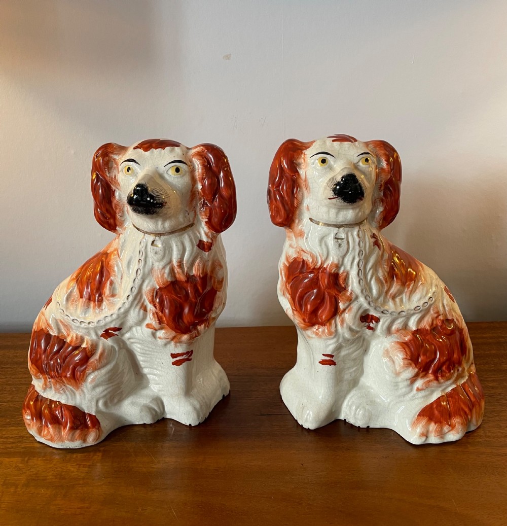 A pair of seated Victorian Staffordshire earthenware spaniel figurines featuring white glazed bodies with rust-red painted patches, black snouts, and gilded collars. View II