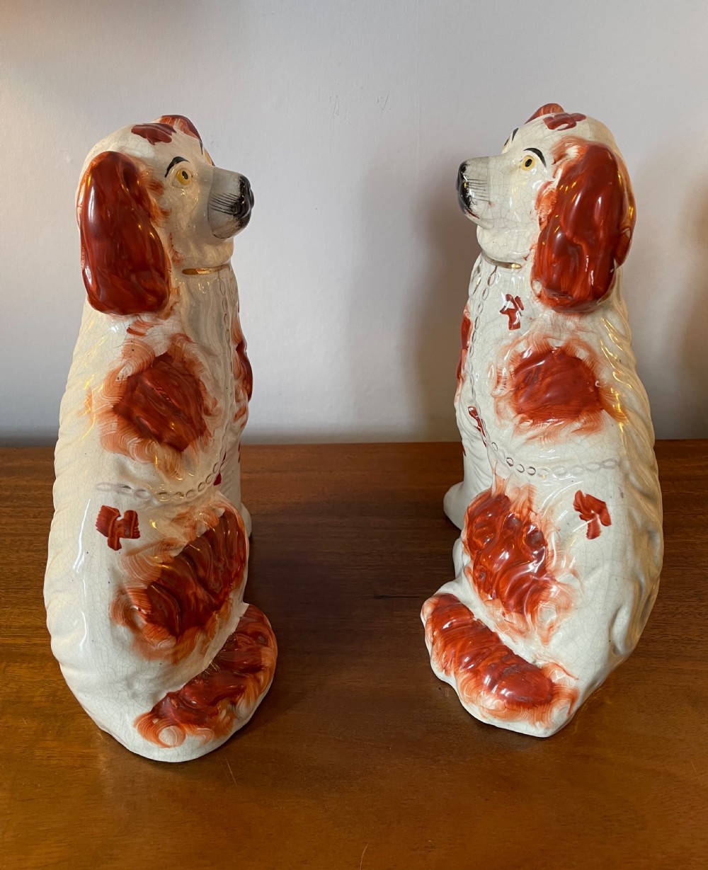 A pair of seated Victorian Staffordshire earthenware spaniel figurines featuring white glazed bodies with rust-red painted patches, black snouts, and gilded collars. View III