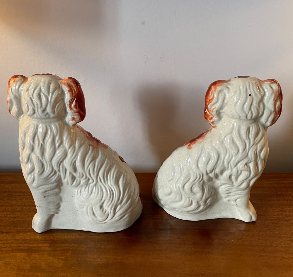 A pair of seated Victorian Staffordshire earthenware spaniel figurines featuring white glazed bodies with rust-red painted patches, black snouts, and gilded collars. View IV