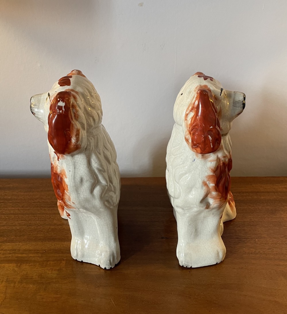 A pair of seated Victorian Staffordshire earthenware spaniel figurines featuring white glazed bodies with rust-red painted patches, black snouts, and gilded collars. View V