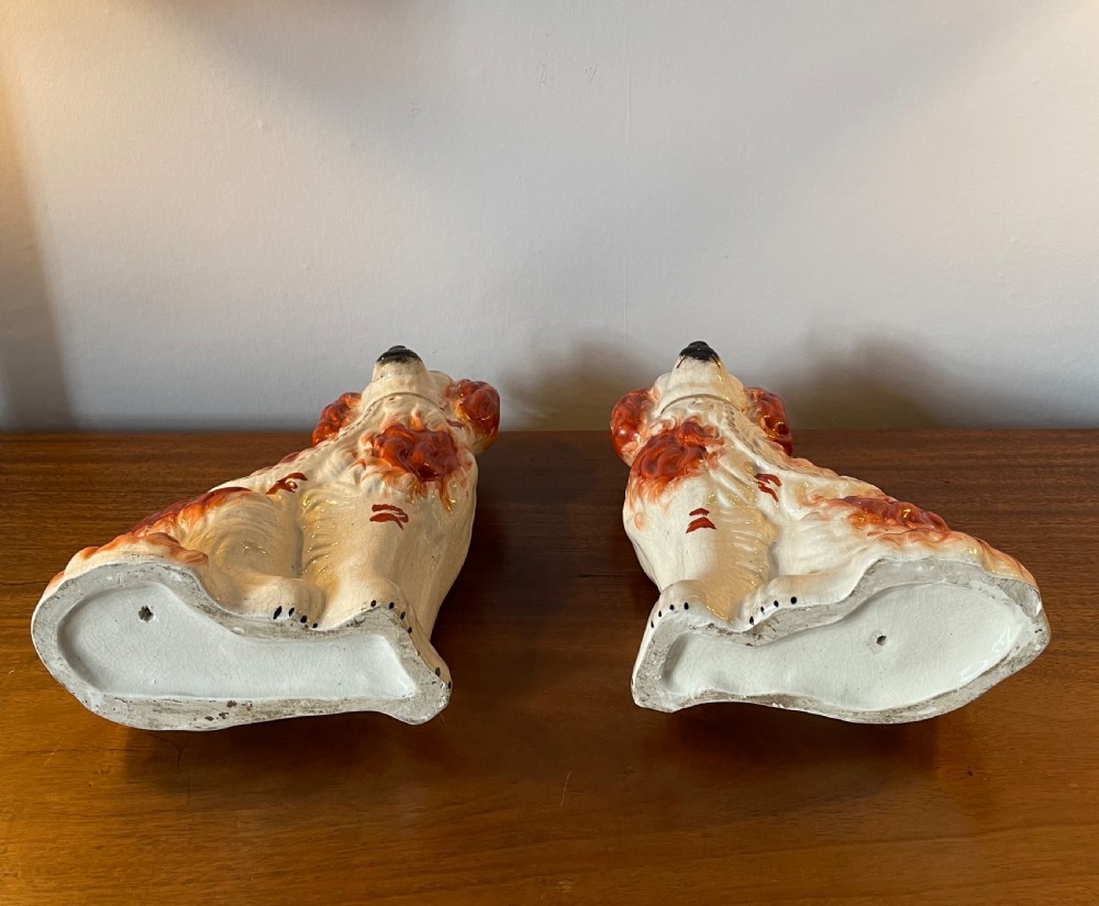 A pair of seated Victorian Staffordshire earthenware spaniel figurines featuring white glazed bodies with rust-red painted patches, black snouts, and gilded collars. View VI