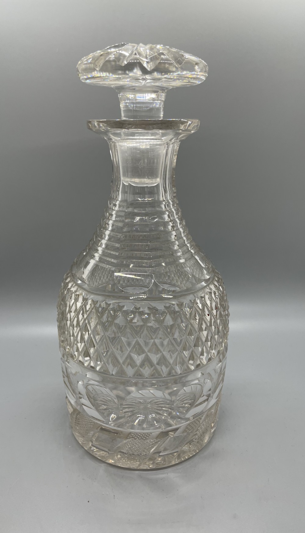 A clear cut lead crystal decanter featuring diamond cutting, a ringed neck, and a star-cut flat stopper.
