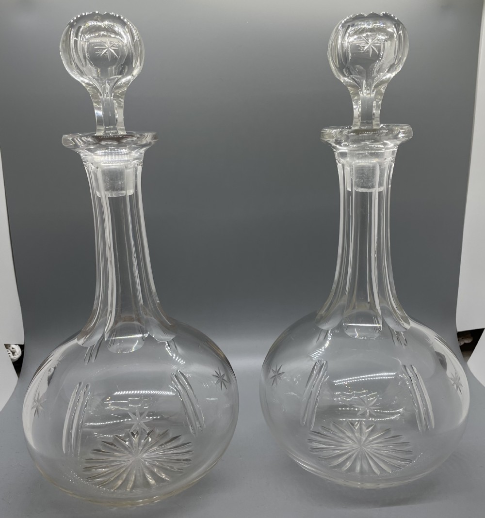 A pair of Victorian clear cut crystal decanters featuring starburst geometric engravings, fluted necks, and matching round cut glass stoppers.