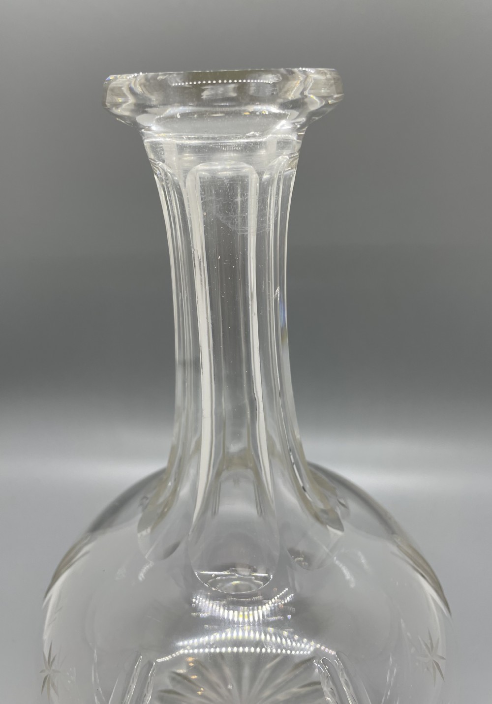 A pair of Victorian clear cut crystal decanters featuring starburst geometric engravings, fluted necks, and matching round cut glass stoppers. View IV