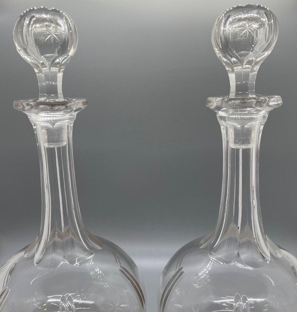 A pair of Victorian clear cut crystal decanters featuring starburst geometric engravings, fluted necks, and matching round cut glass stoppers. View VI