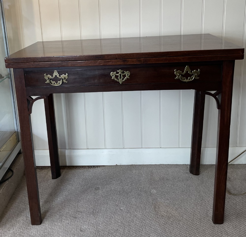 A Georgian mahogany fold-over tea table featuring straight square legs with subtle corner brackets and brass drop handles.