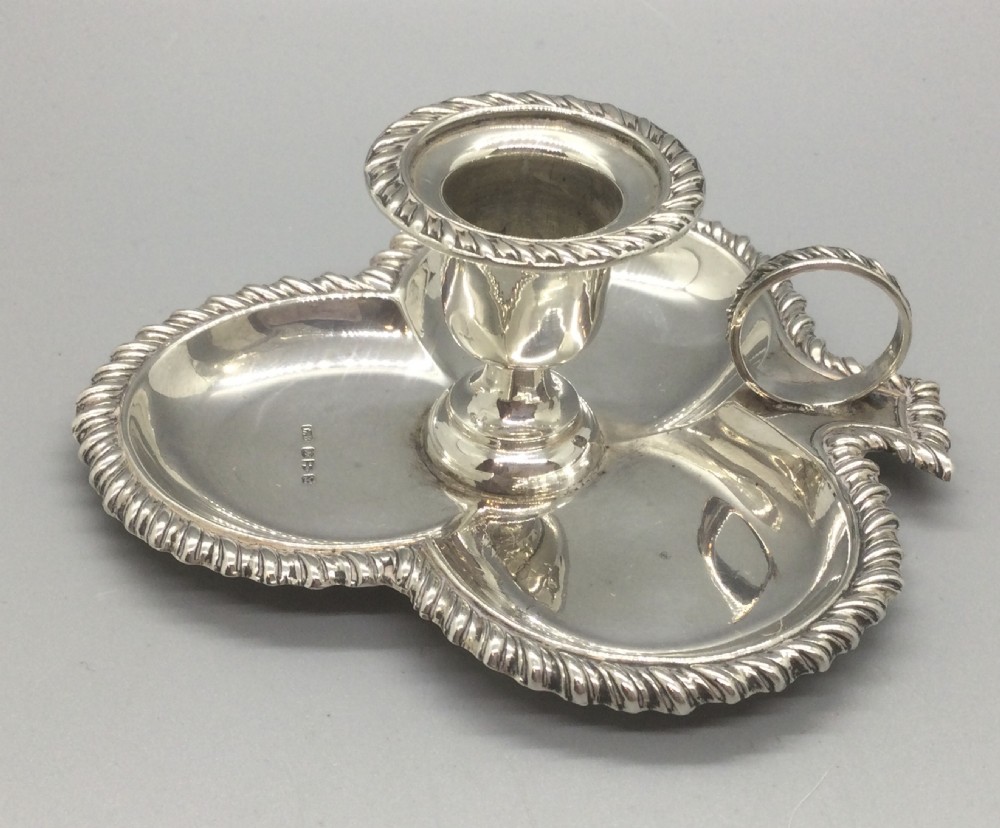 An antique sterling silver chamberstick featuring a trefoil-shaped tray base with a gadrooned rim, a central candle sconce, and a finger ring handle.