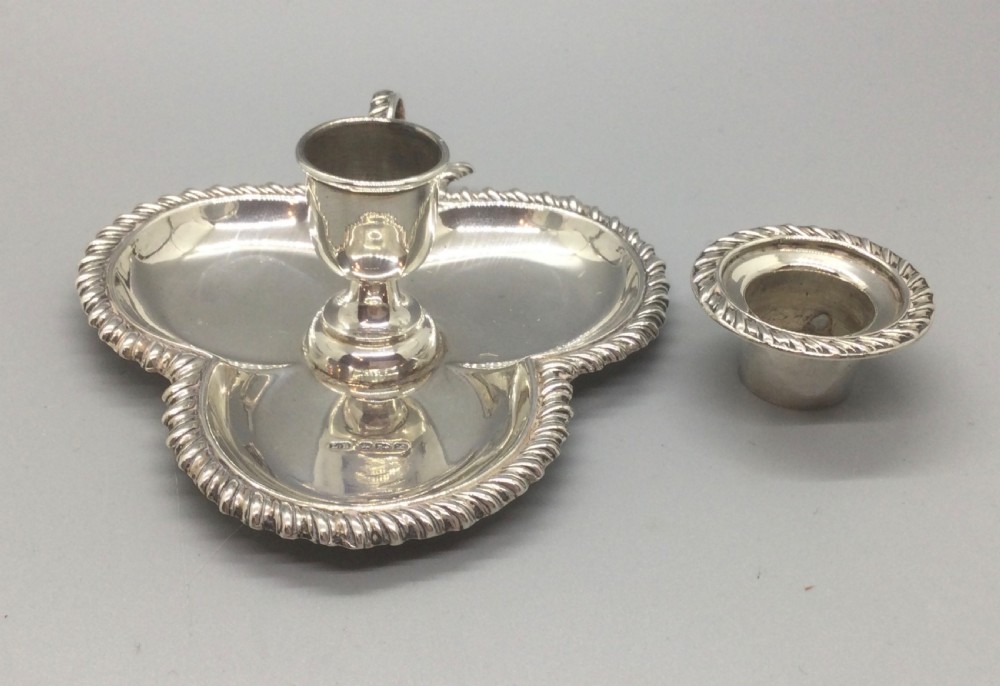 An antique sterling silver chamberstick featuring a trefoil-shaped tray base with a gadrooned rim, a central candle sconce, and a finger ring handle. View V