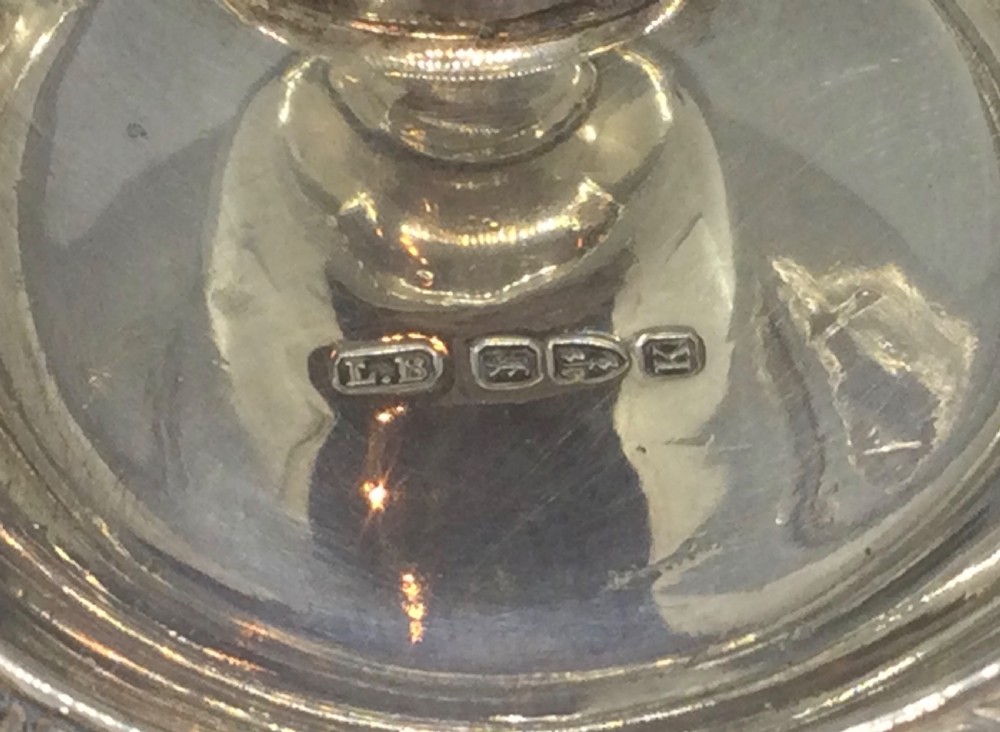 An antique sterling silver chamberstick featuring a trefoil-shaped tray base with a gadrooned rim, a central candle sconce, and a finger ring handle. View VI