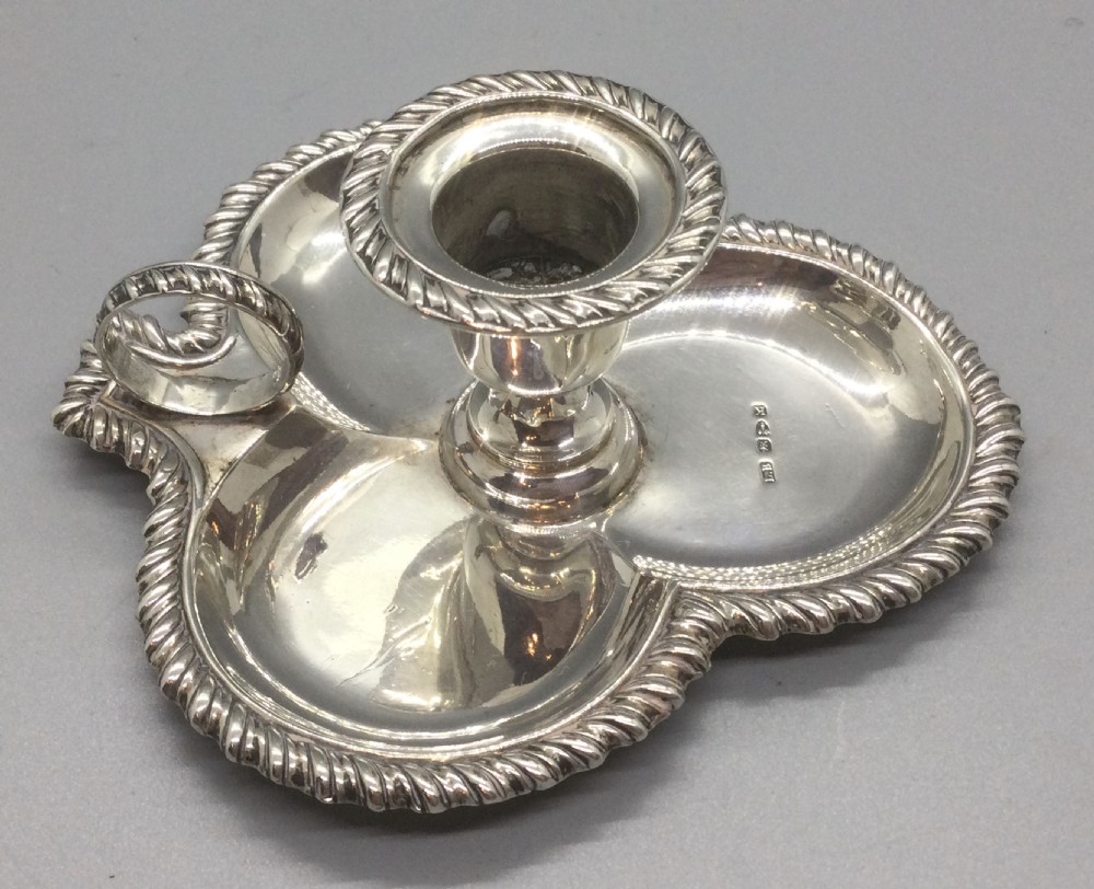 An antique sterling silver chamberstick featuring a trefoil-shaped tray base with a gadrooned rim, a central candle sconce, and a finger ring handle. View VIII