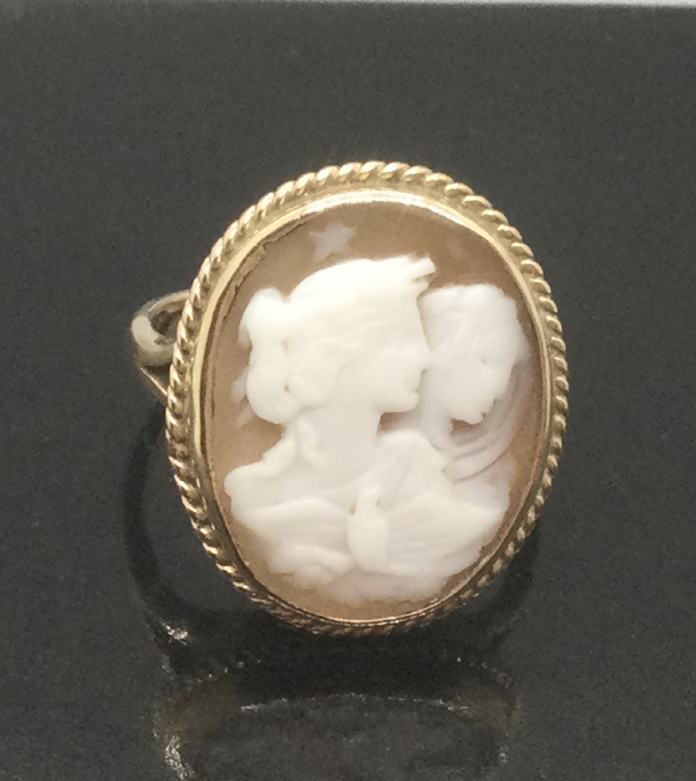 An oval Victorian 9ct yellow gold ring containing a carved shell cameo with two classical female profiles surrounded by a twisted rope border.