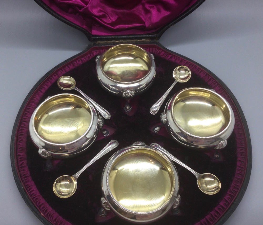 A set of four Victorian sterling silver open salt cellars with gilt interiors and shell-capped feet, displayed in a velvet-lined case with spoons. View III