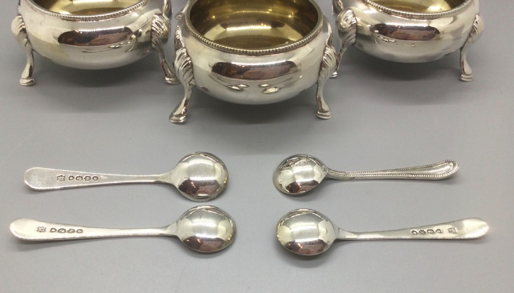 A set of four Victorian sterling silver open salt cellars with gilt interiors and shell-capped feet, displayed in a velvet-lined case with spoons. View V