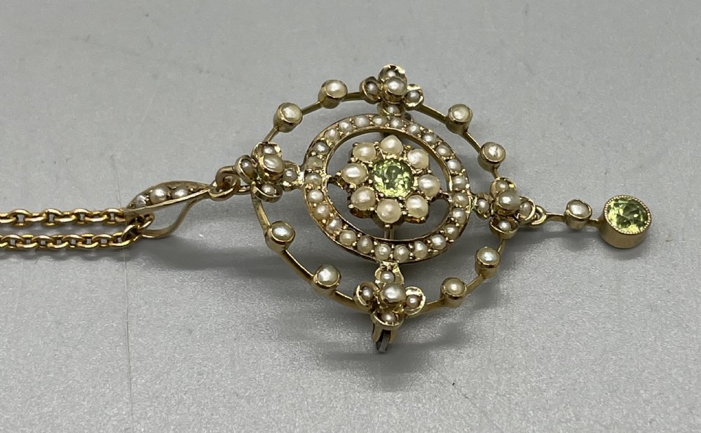 An Edwardian 9ct gold circular openwork pendant set with seed pearls and round faceted peridots, featuring a hanging drop gemstone and attached chain. View III