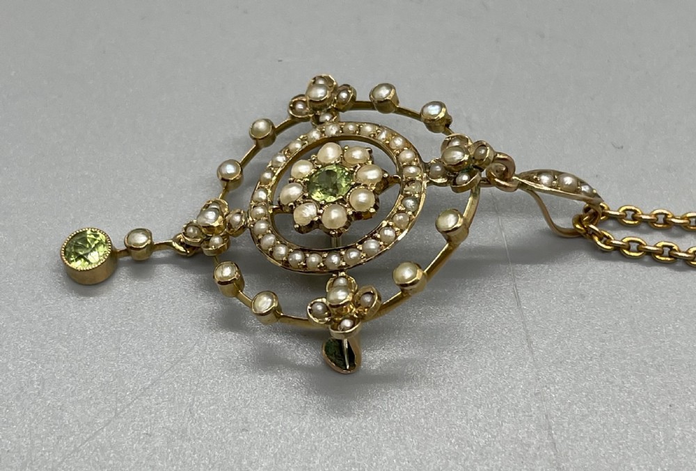 An Edwardian 9ct gold circular openwork pendant set with seed pearls and round faceted peridots, featuring a hanging drop gemstone and attached chain. View V