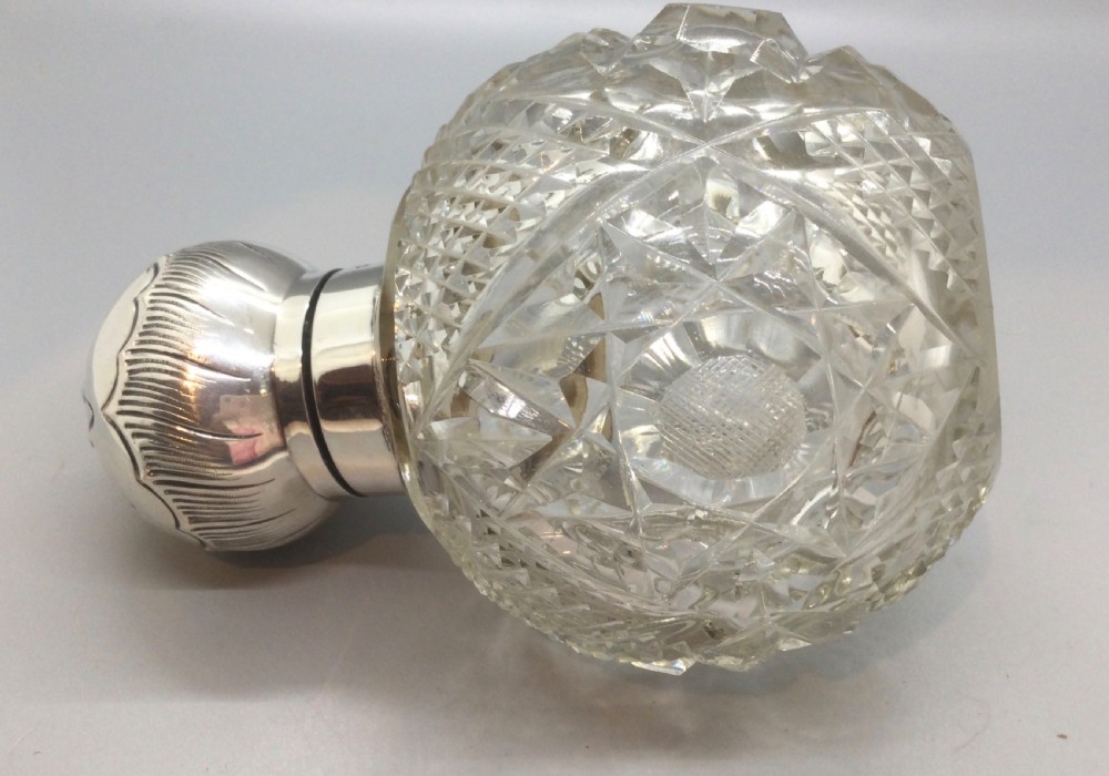 A globular cut glass perfume bottle featuring a faceted diamond pattern and an embossed sterling silver top. View IX
