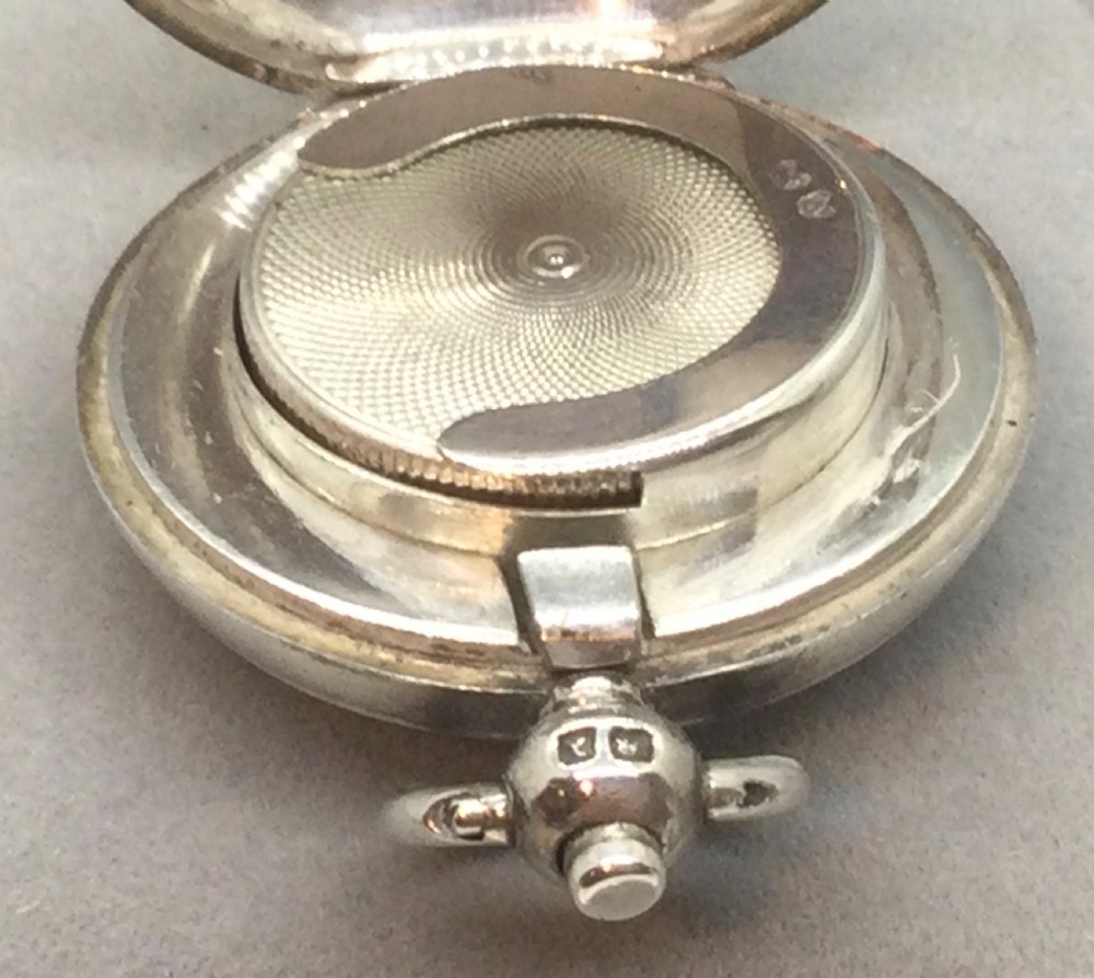 A circular Victorian sterling silver sovereign case featuring hand-engraved foliate motifs, a central monogram cartouche, and a top suspension ring. View VII