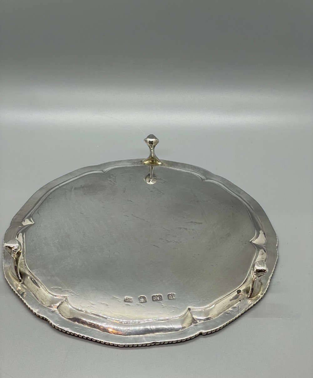 A circular Georgian sterling silver salver featuring a shaped gadrooned rim, an engraved central monogram, and three cast feet. View VI