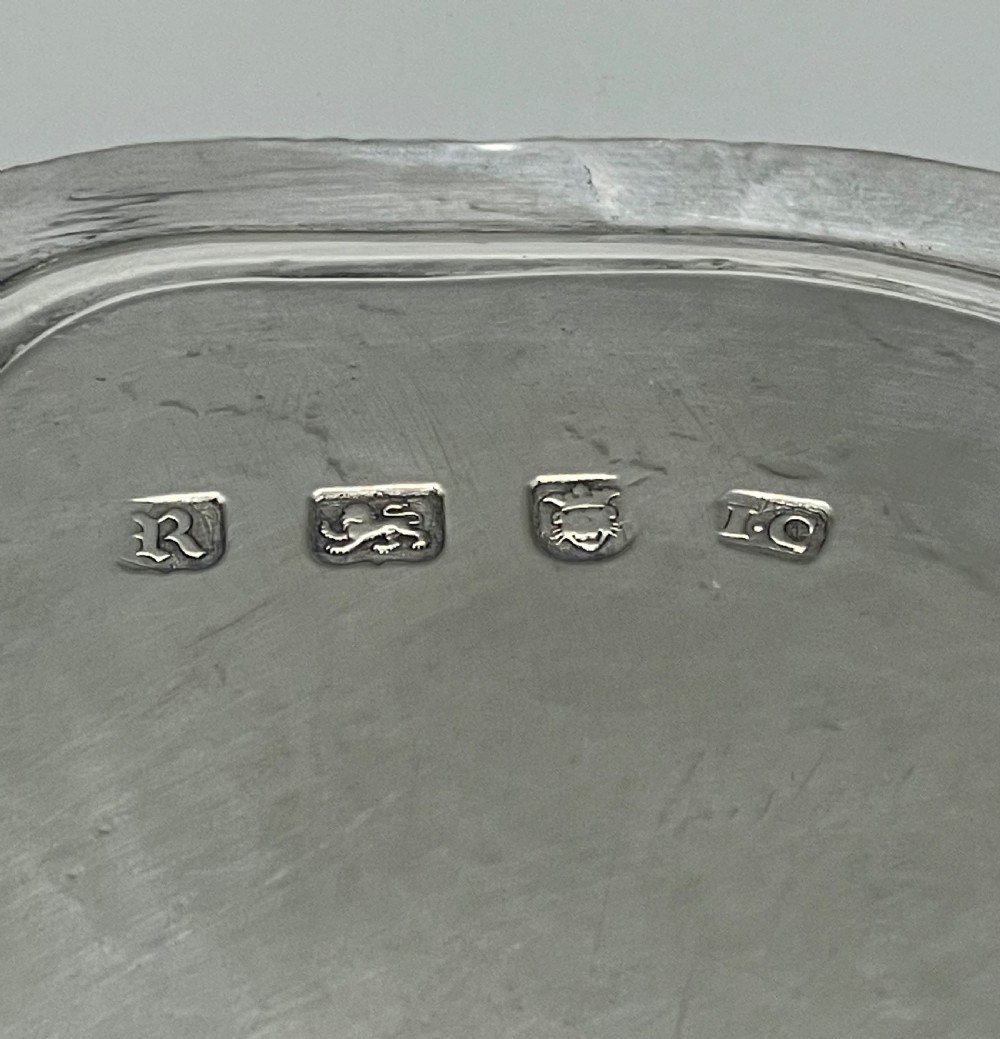 A circular Georgian sterling silver salver featuring a shaped gadrooned rim, an engraved central monogram, and three cast feet. View XX