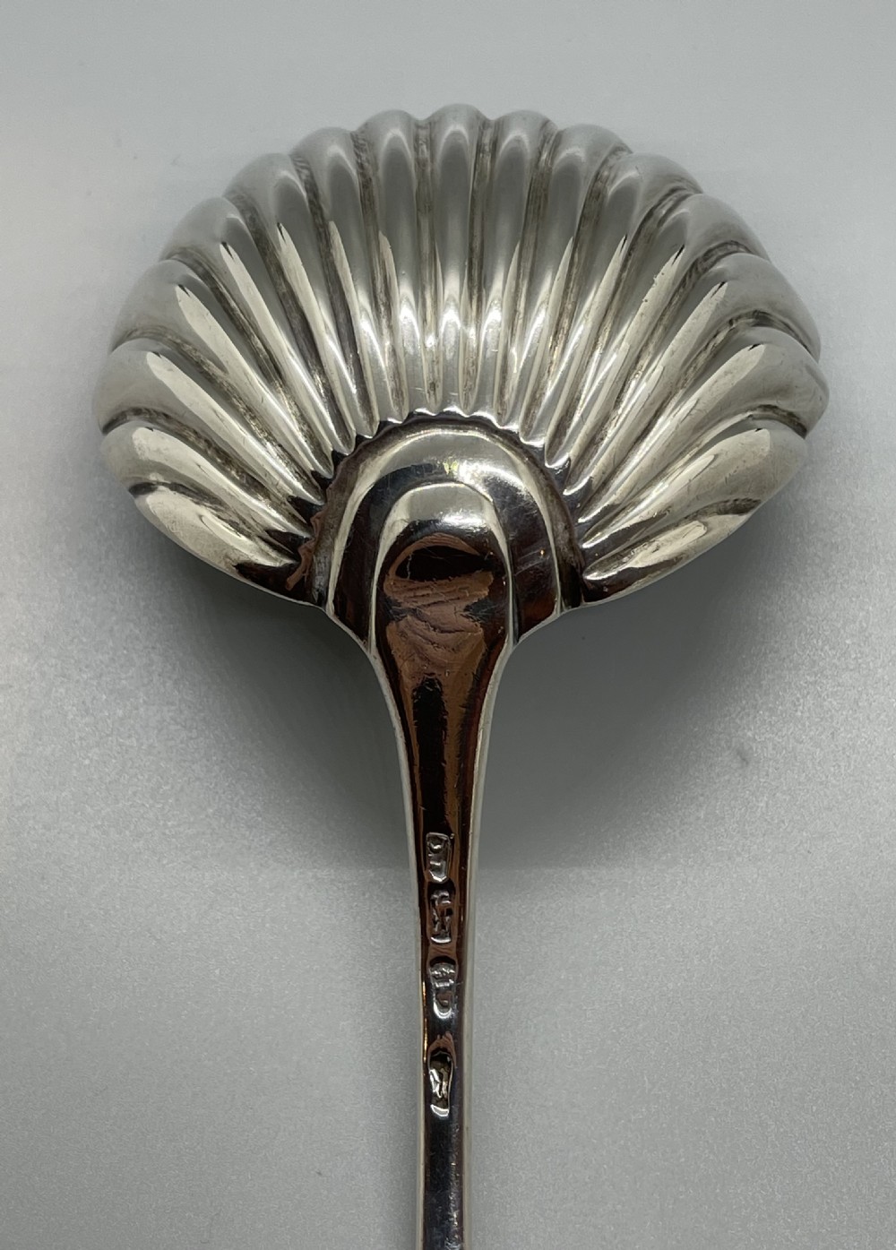 An 18th-century sterling silver soup ladle featuring a fluted shell-shaped bowl and an engraved curved handle terminal. View VII