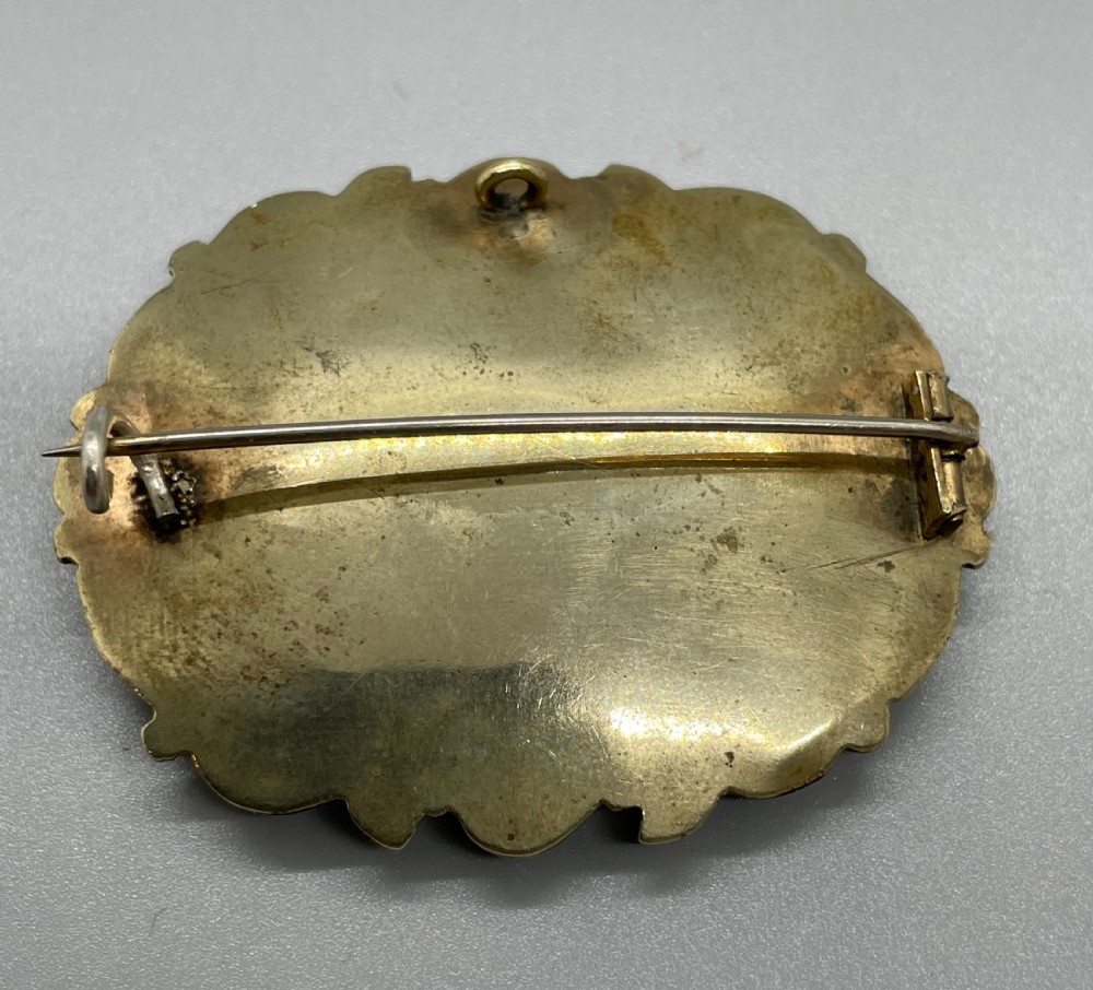 An oval early Victorian gold mourning brooch featuring a scrollwork frame, black enamel border with lettering, and a glass compartment containing woven hair. View IV