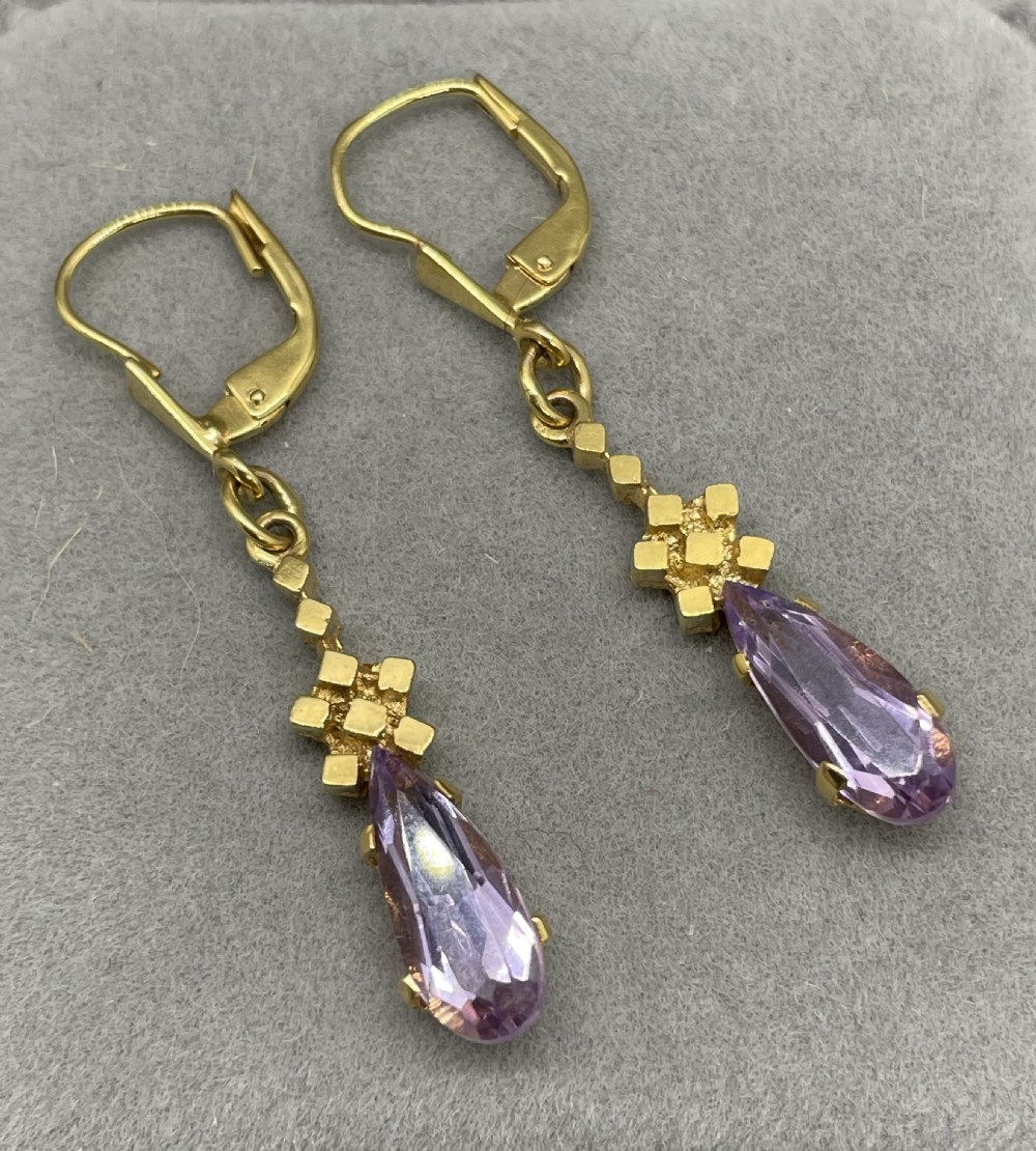 A pair of 1960s 9ct gold drop earrings featuring lever-back fastenings, textured geometric links, and pear-cut purple amethyst stones in claw settings.