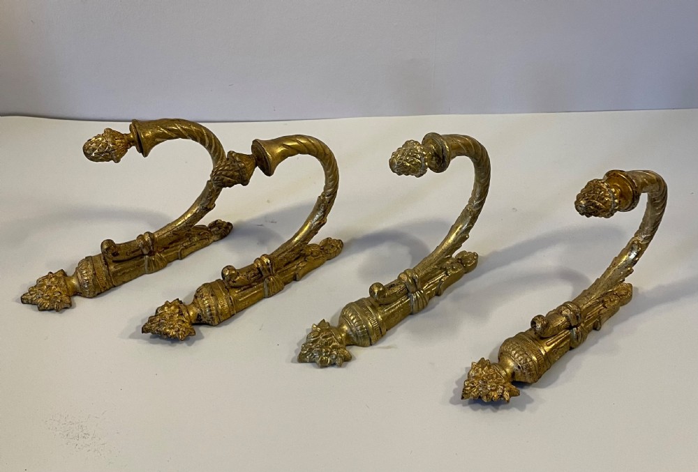 A set of four 19th-century French ormolu curtain tie backs with pinecone finials, fluted arms, and wall-mount backplates.