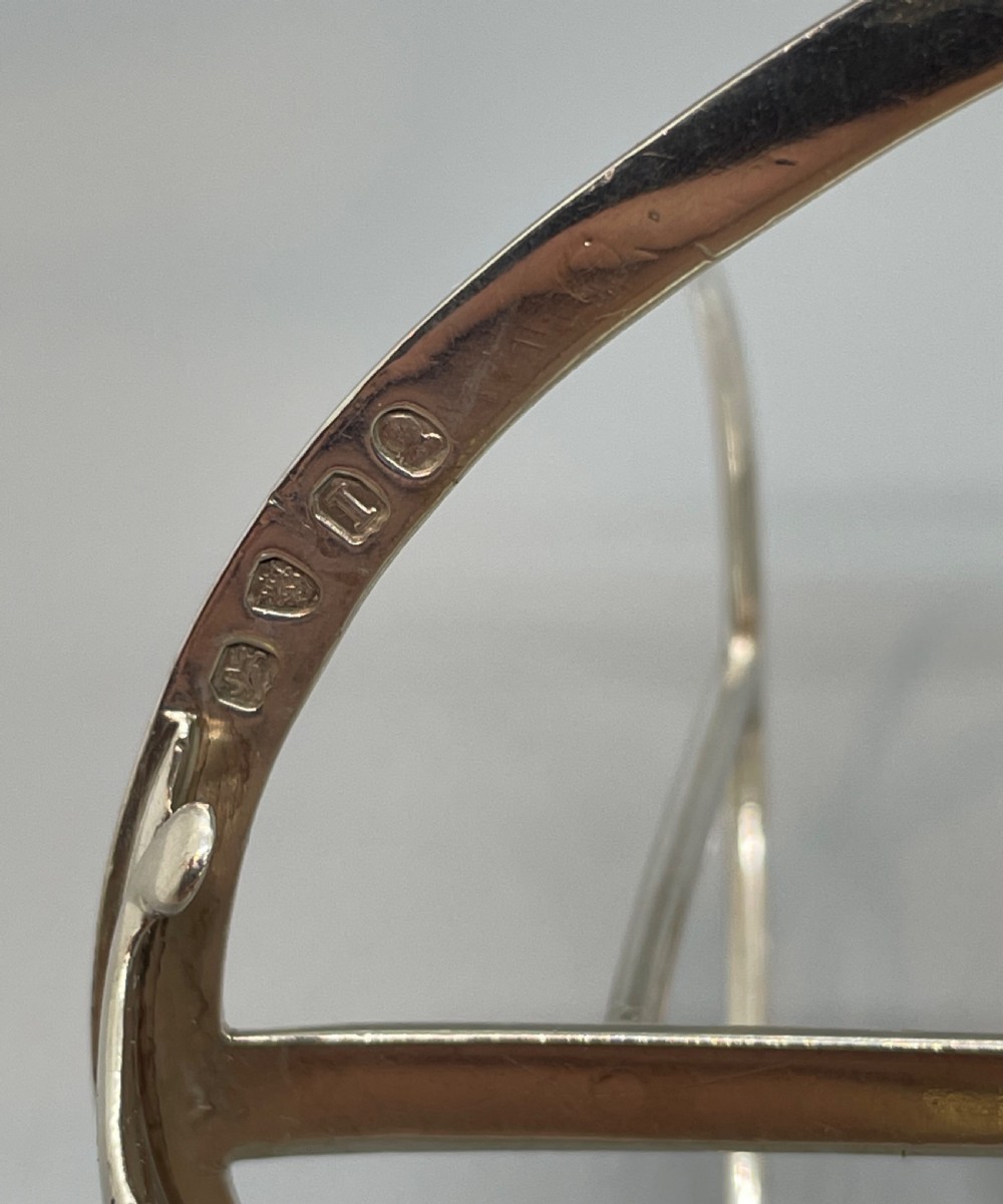 A George III sterling silver toast rack featuring seven arched divisions, an oval base frame, bracket feet, and a central ring handle. View VI