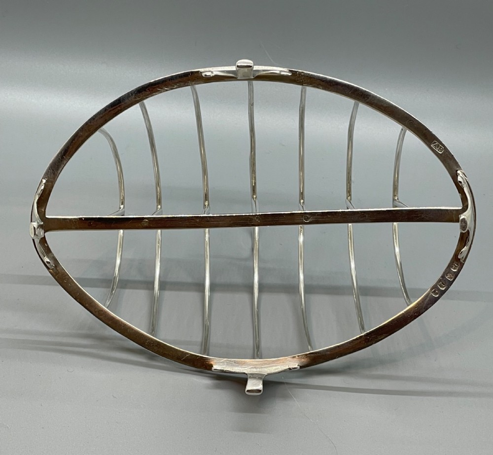 A George III sterling silver toast rack featuring seven arched divisions, an oval base frame, bracket feet, and a central ring handle. View VIII