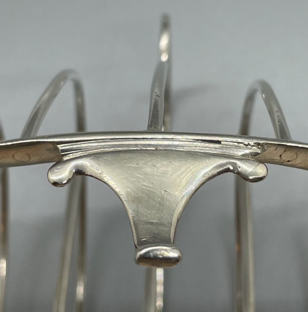 A George III sterling silver toast rack featuring seven arched divisions, an oval base frame, bracket feet, and a central ring handle. View IX
