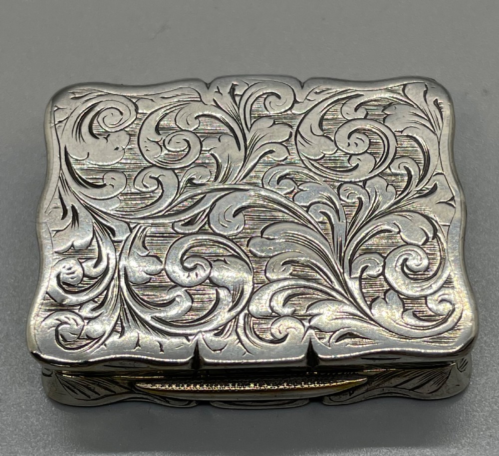 An early Victorian rectangular sterling silver vinaigrette box with scrollwork engraving, shaped edges, and a central monogrammed cartouche. View II