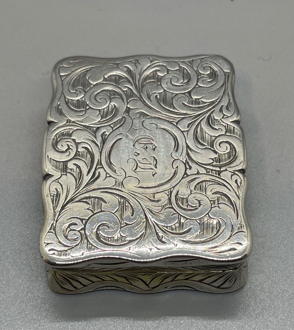An early Victorian rectangular sterling silver vinaigrette box with scrollwork engraving, shaped edges, and a central monogrammed cartouche. View IV