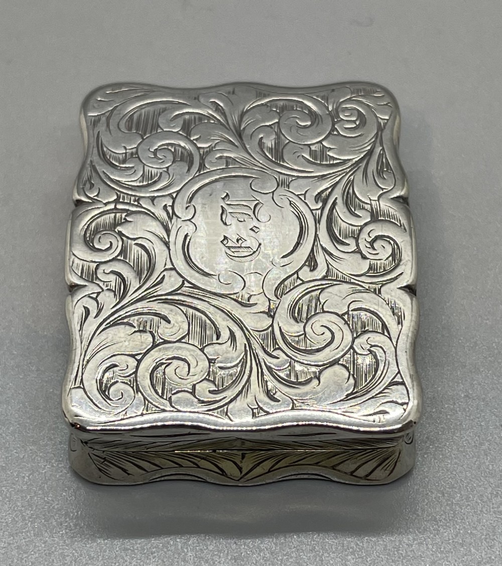 An early Victorian rectangular sterling silver vinaigrette box with scrollwork engraving, shaped edges, and a central monogrammed cartouche. View V