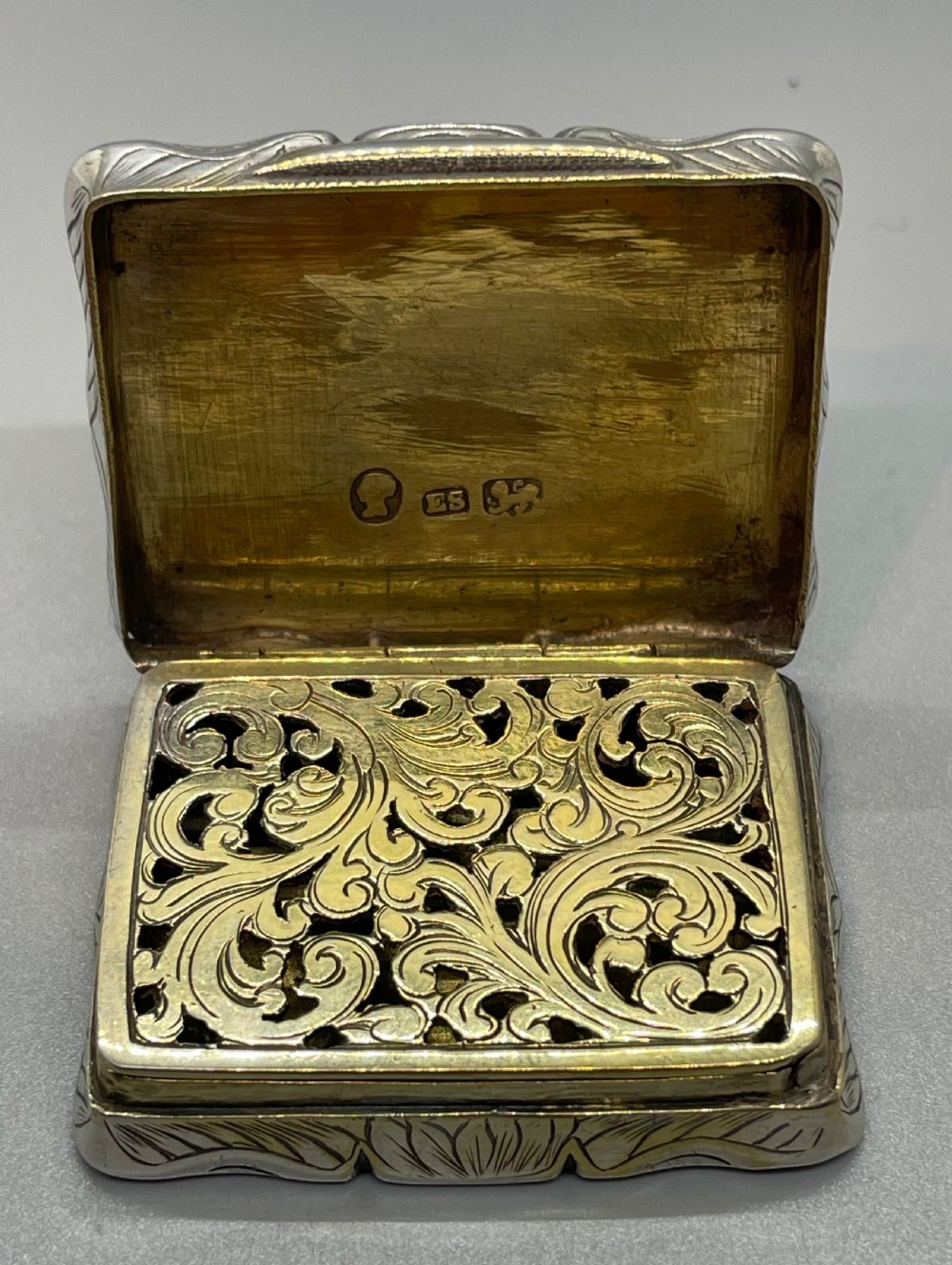 An early Victorian rectangular sterling silver vinaigrette box with scrollwork engraving, shaped edges, and a central monogrammed cartouche. View VI