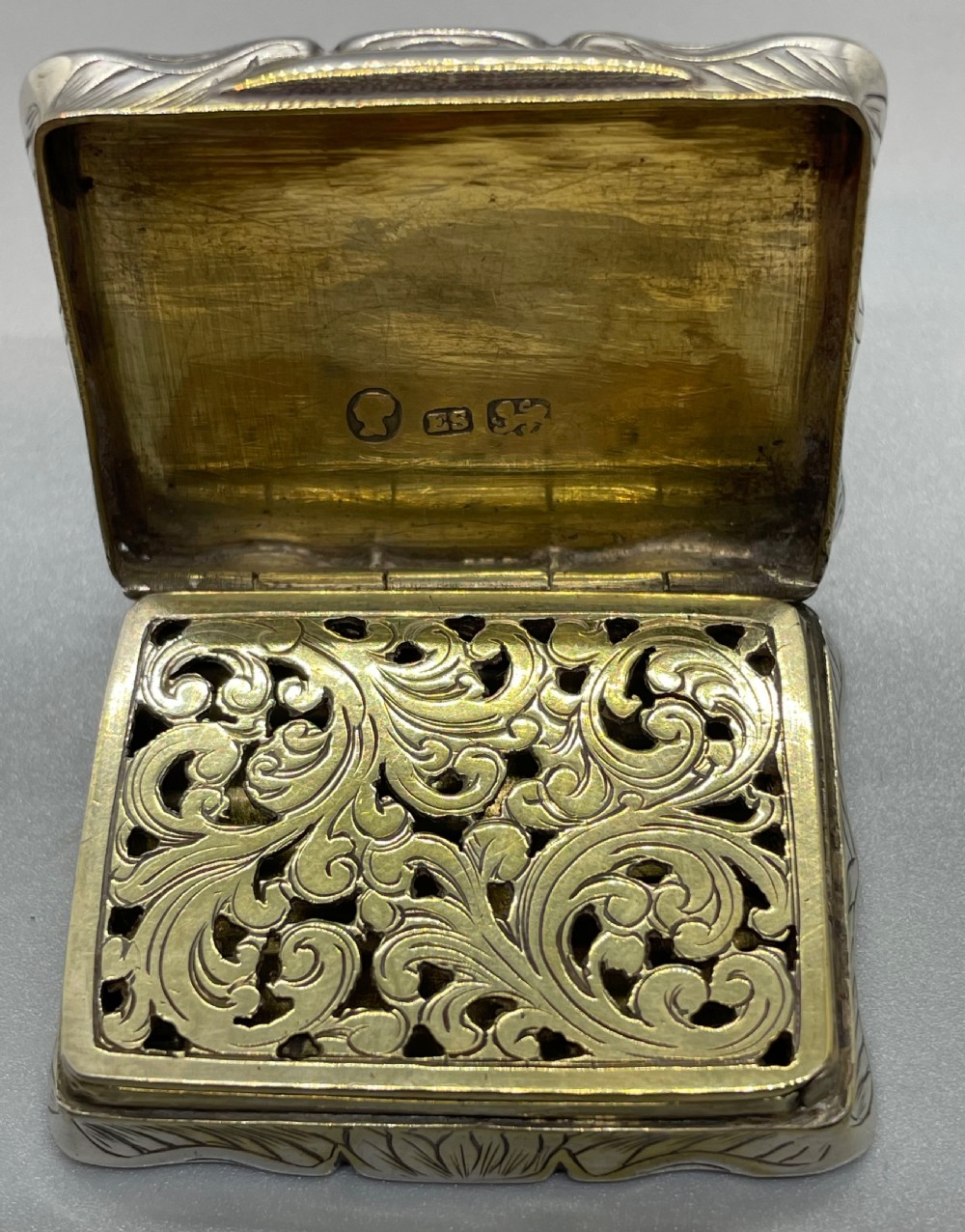An early Victorian rectangular sterling silver vinaigrette box with scrollwork engraving, shaped edges, and a central monogrammed cartouche. View IX