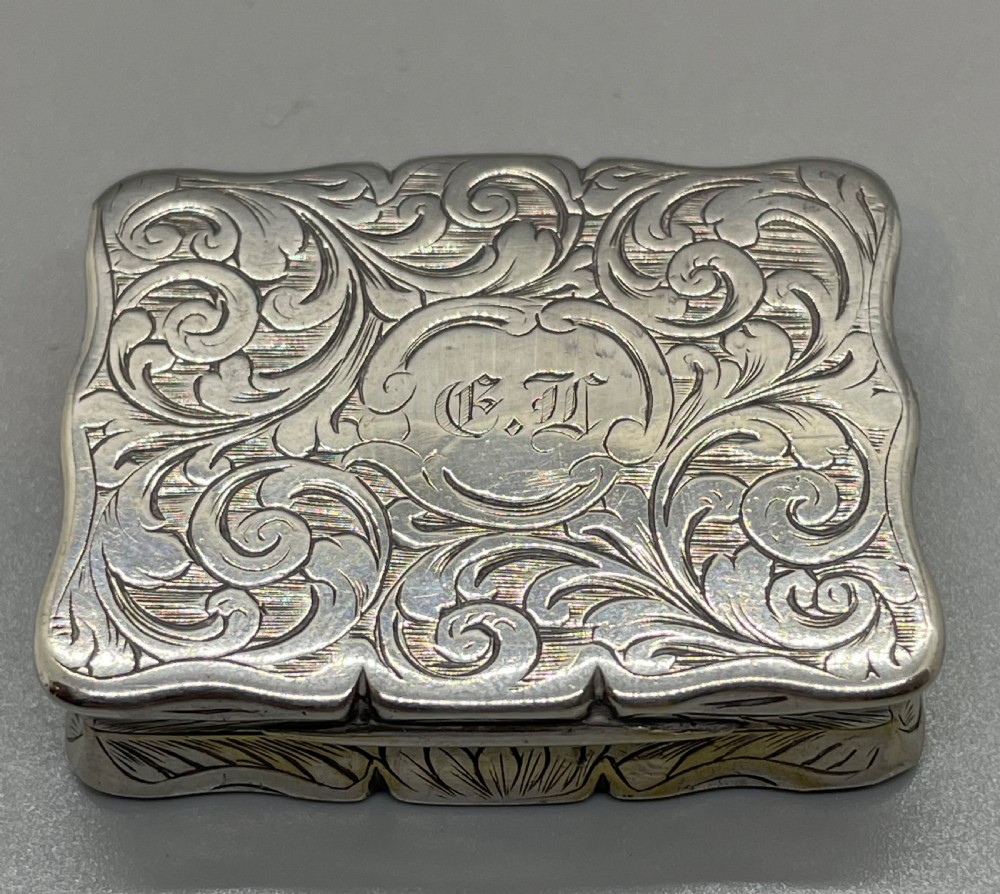 An early Victorian rectangular sterling silver vinaigrette box with scrollwork engraving, shaped edges, and a central monogrammed cartouche. View X