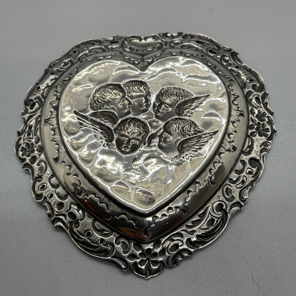A late Victorian heart-shaped sterling silver trinket dish featuring an embossed central motif of cherub heads amongst clouds with a pierced scroll border. View III