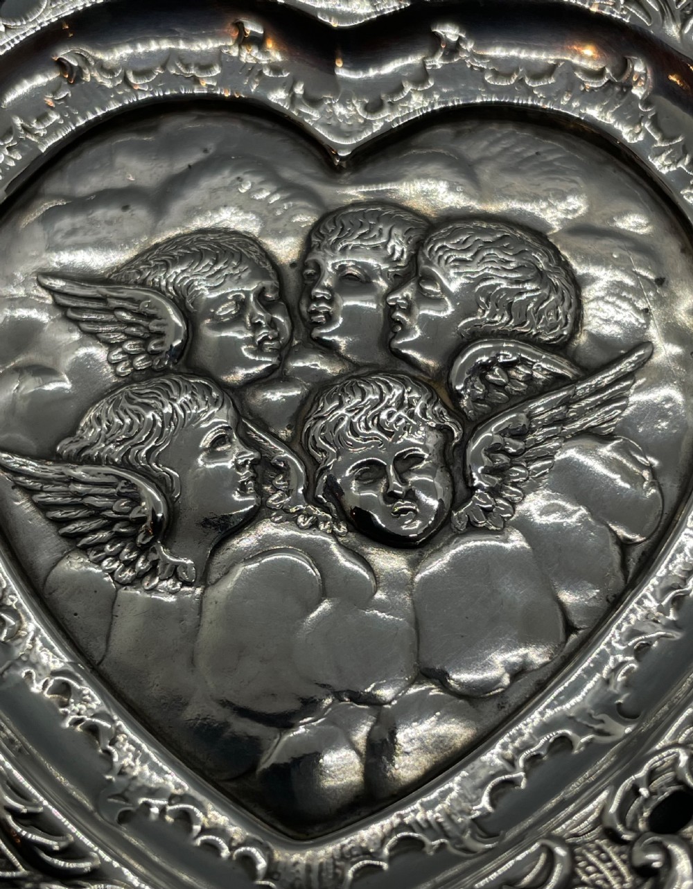 A late Victorian heart-shaped sterling silver trinket dish featuring an embossed central motif of cherub heads amongst clouds with a pierced scroll border. View V