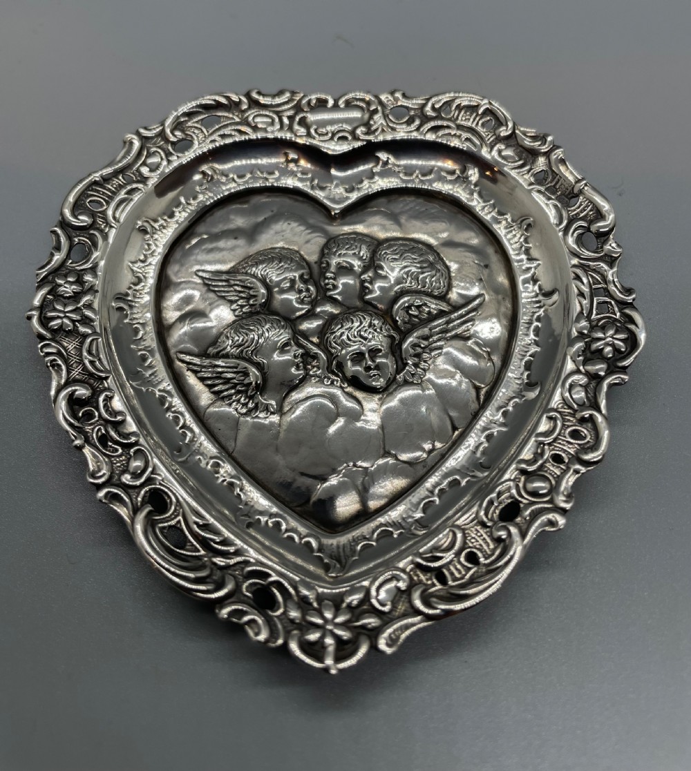 A late Victorian heart-shaped sterling silver trinket dish featuring an embossed central motif of cherub heads amongst clouds with a pierced scroll border. View VII