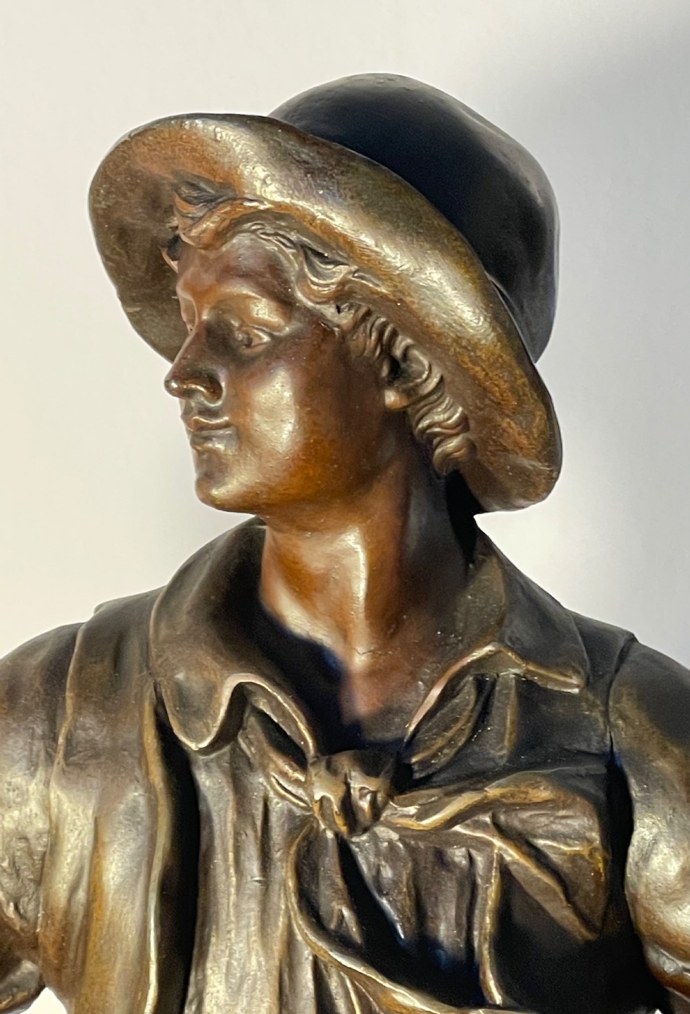 A dark patinated bronze figure depicting a standing woodsman holding an axe on a circular cast base with a named plaque. View II