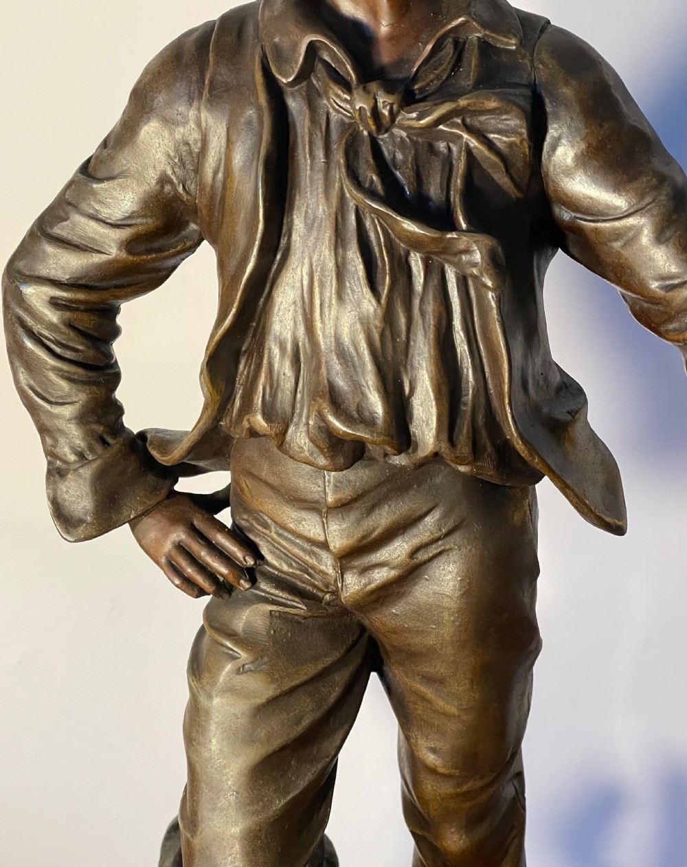 A dark patinated bronze figure depicting a standing woodsman holding an axe on a circular cast base with a named plaque. View III