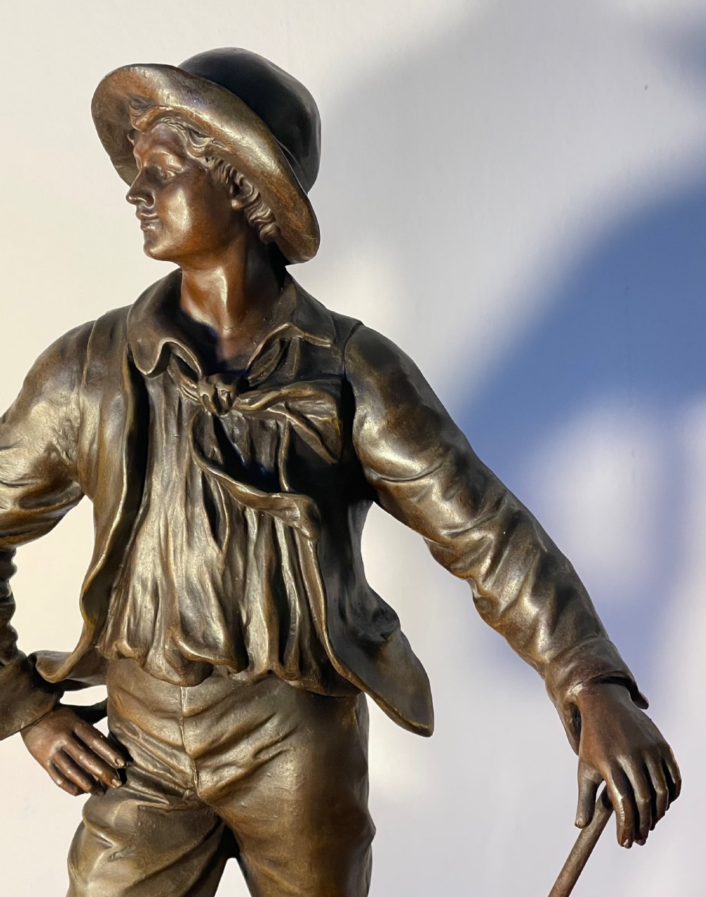 A dark patinated bronze figure depicting a standing woodsman holding an axe on a circular cast base with a named plaque. View IV