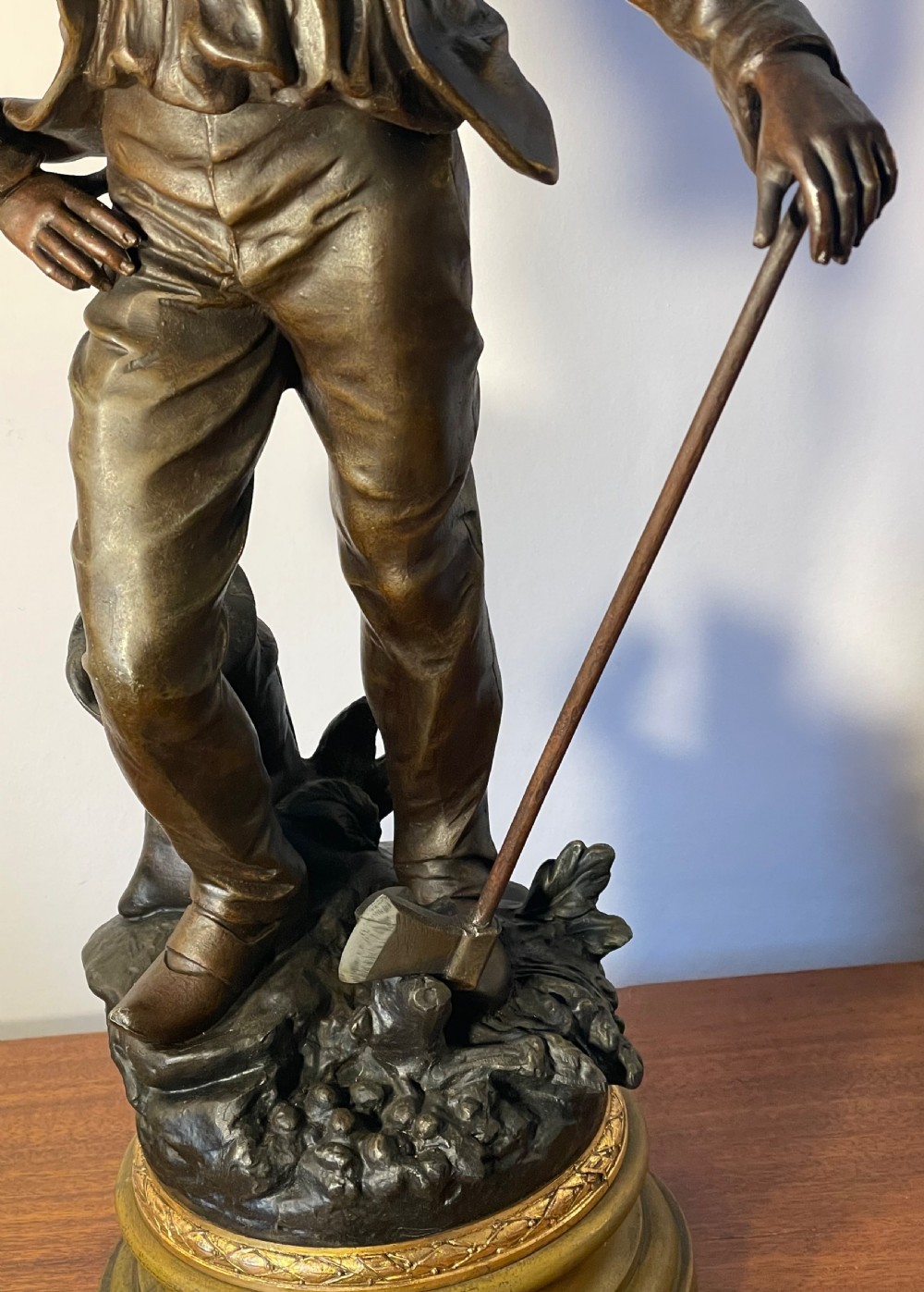 A dark patinated bronze figure depicting a standing woodsman holding an axe on a circular cast base with a named plaque. View V
