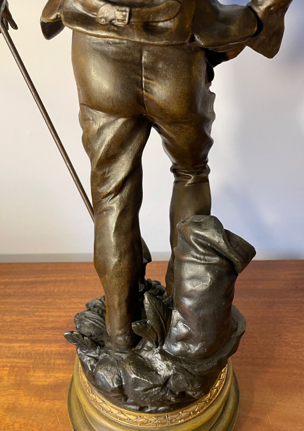 A dark patinated bronze figure depicting a standing woodsman holding an axe on a circular cast base with a named plaque. View X