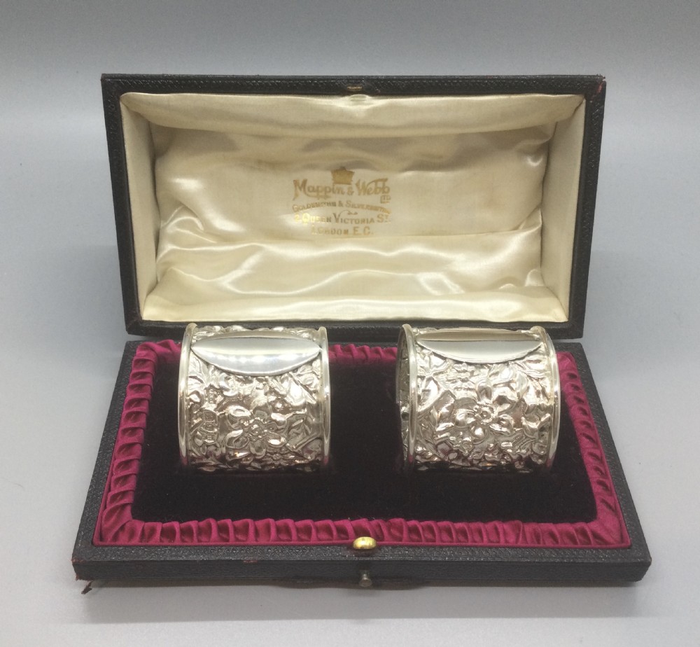 A pair of cased Victorian sterling silver napkin rings with chased floral decoration and plain oval cartouches.