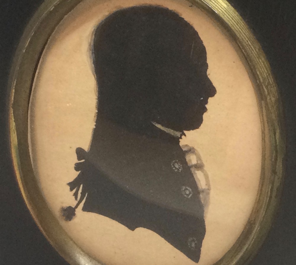 An antique Georgian oval silhouette portrait of a gentleman in profile, housed within a dark rectangular ebonised frame featuring a brass acorn hanger. View V