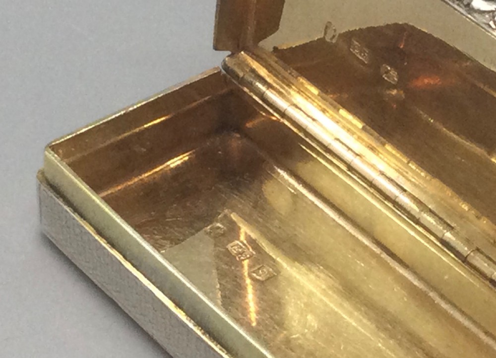A rectangular Georgian sterling silver snuff box displaying geometric engine-turned engraving, a plain rectangular cartouche, and a chased silver thumbpiece. View IX