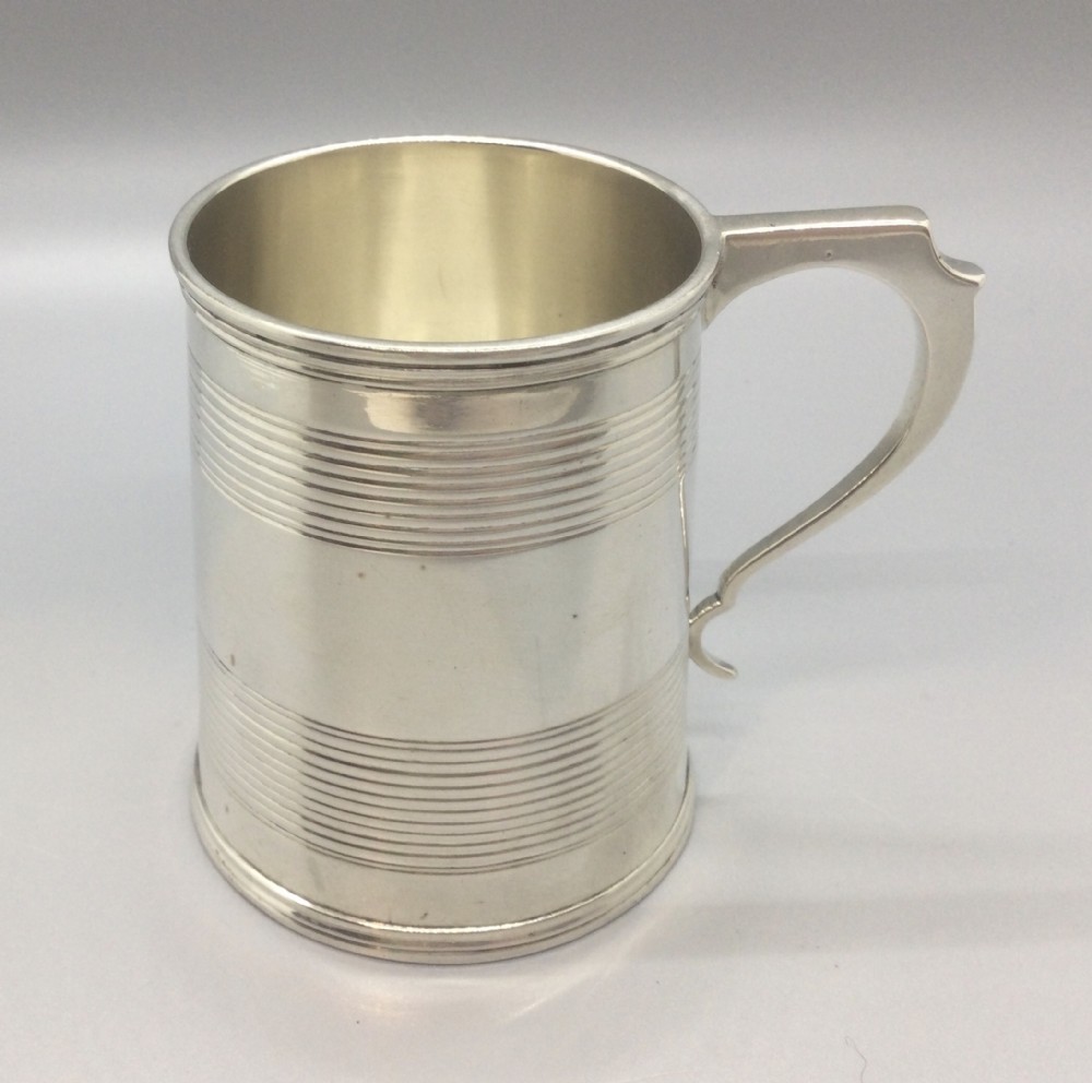 A cylindrical sterling silver christening mug featuring horizontal reeded banding and an angular curved handle.