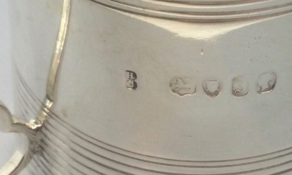 A cylindrical sterling silver christening mug featuring horizontal reeded banding and an angular curved handle. View IX