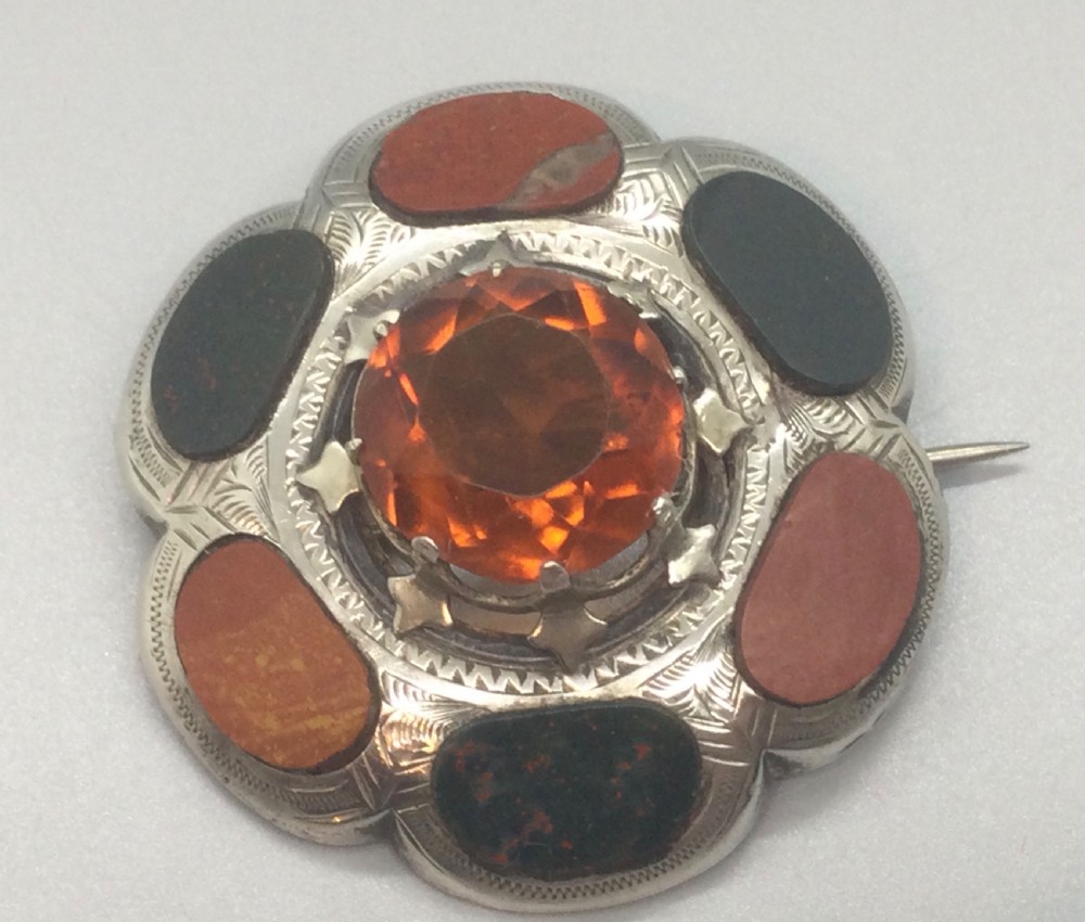 A circular Victorian Scottish silver brooch featuring an engraved scalloped border inlaid with agate stones and set with a central faceted orange citrine. View IV